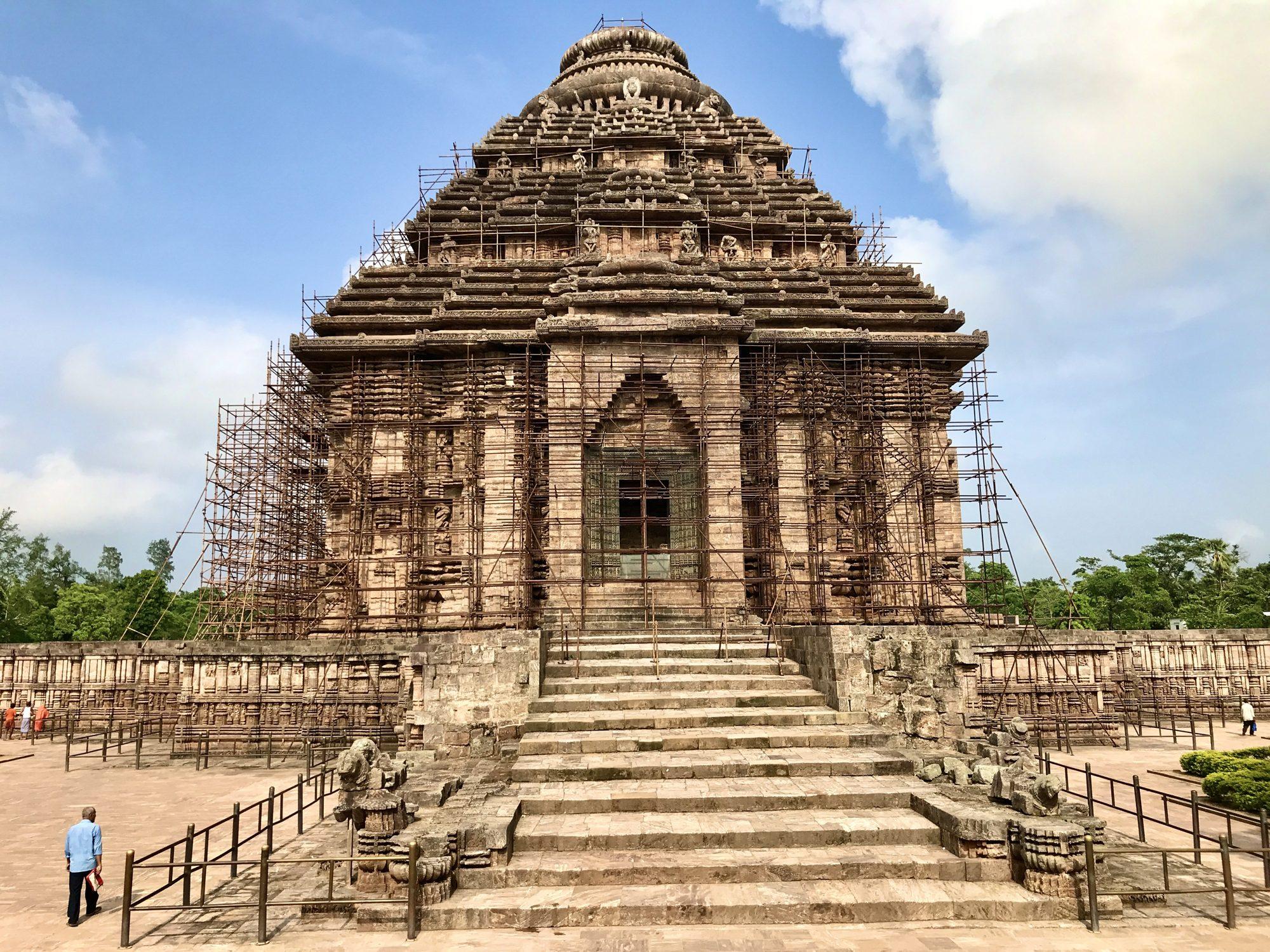 The Konark Sun Temple in Odisha seen from the front steps under a blue sky, partly under restoration scaffolding