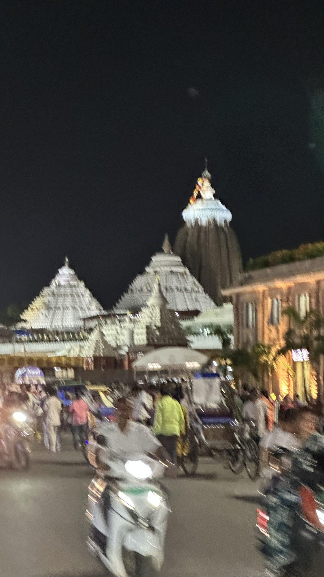 A street in Puri at night in front of the lit Jagannath Temple with scooters and rickshaws